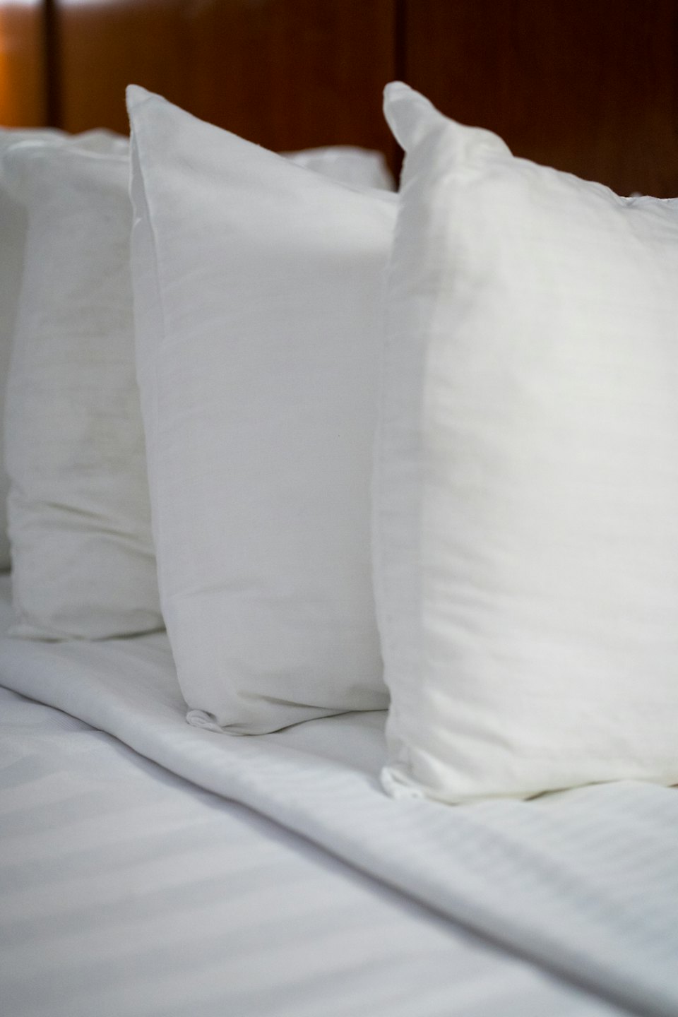 Three plump white pillows resting on crisp striped bed sheets.
