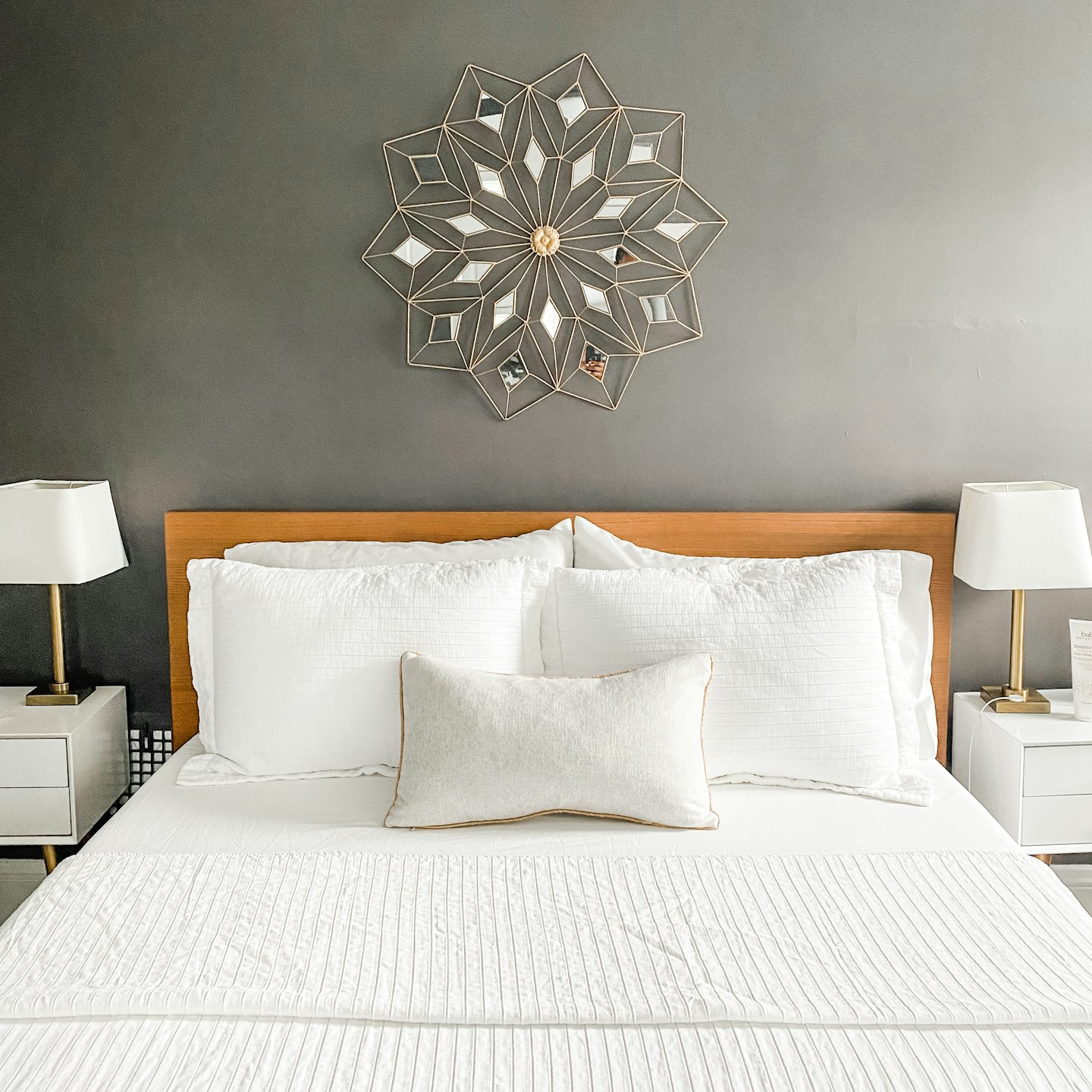 A modern bedroom with white bedding and gold wall art.